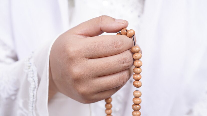 A person's hands holding a tasbih (prayer beads), symbolizing the spiritual benefits of reciting Quranic verses. The beads are delicately strung and the hands are engaged in the rhythmic act of counting and reciting, reflecting a serene and contemplative atmosphere.