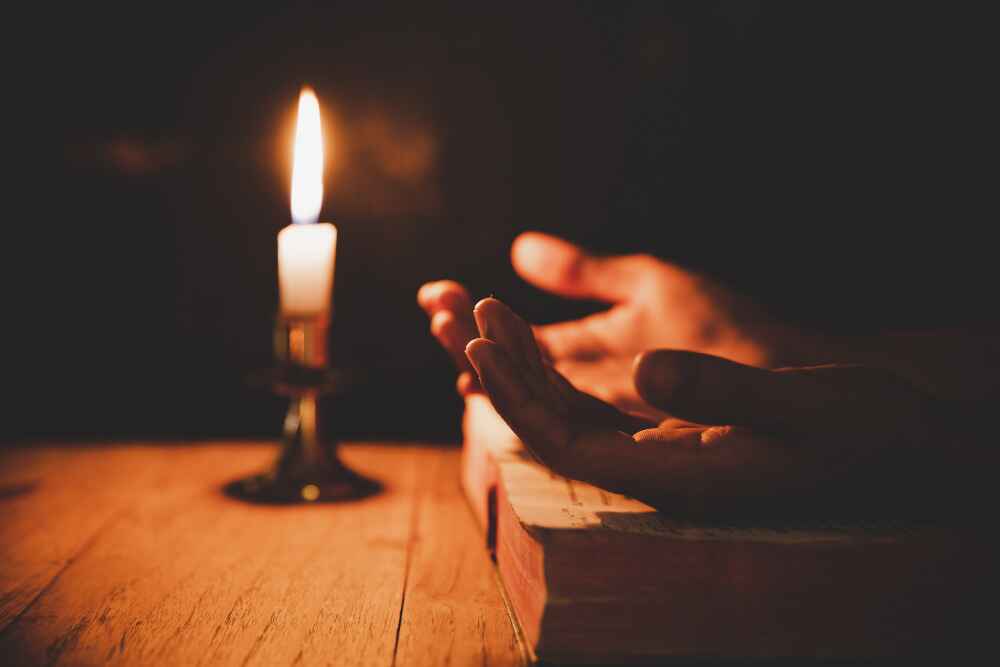 A pair of hands in prayer position and a softly glowing candle, symbolizing the pursuit of tranquility and the potential cure for insomnia in the teachings of the Quran.